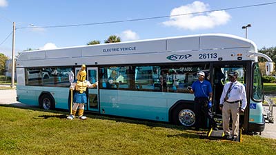 Titus the Titan mascot stands in front of an electric Pinellas Suncoast Transit Authority bus