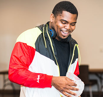 photo of student in a red, white and black jacket smiling, doing an experiment with a bag of ice in a plastic bag