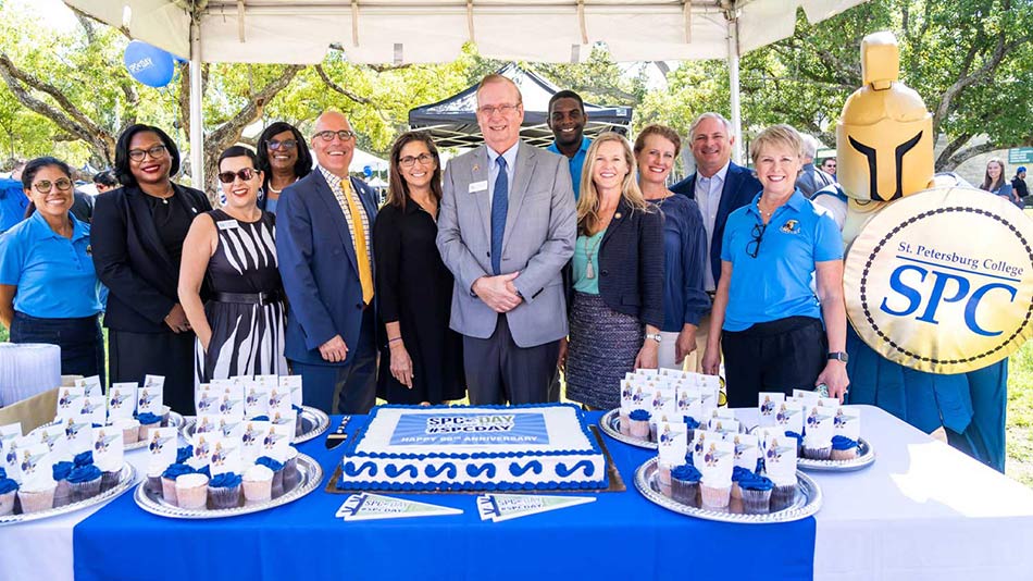 SPC day gathering in front of table with cake and promo items