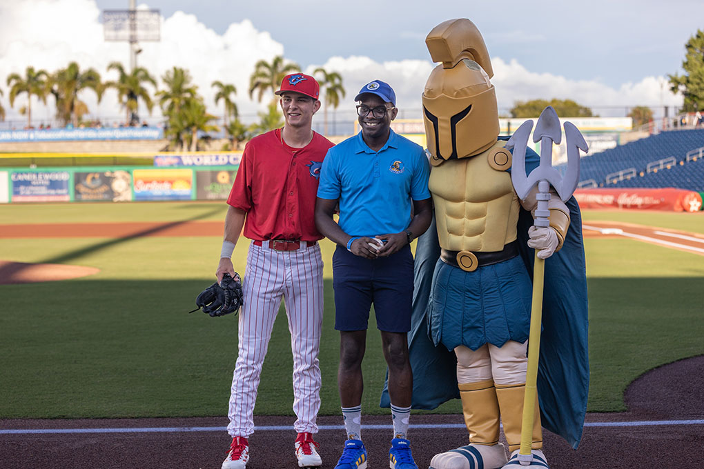 At SPC Day 2025's Night at the Threshers event, a man wearing SPC gear poses with a Threshers player and Titus the Titan.