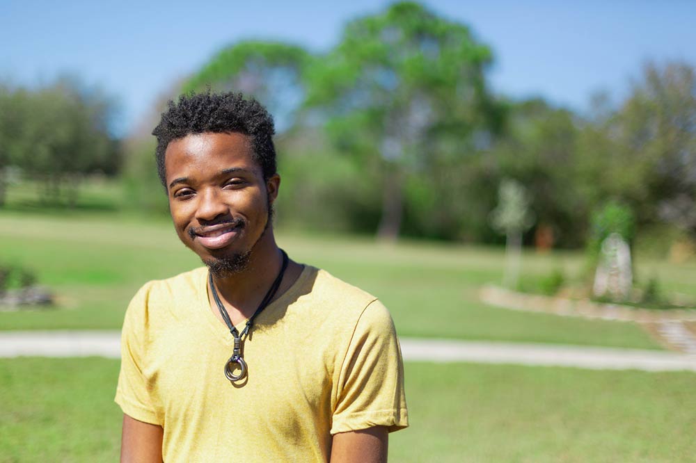 male student wearing a yellow polo shirt smiling at the camera