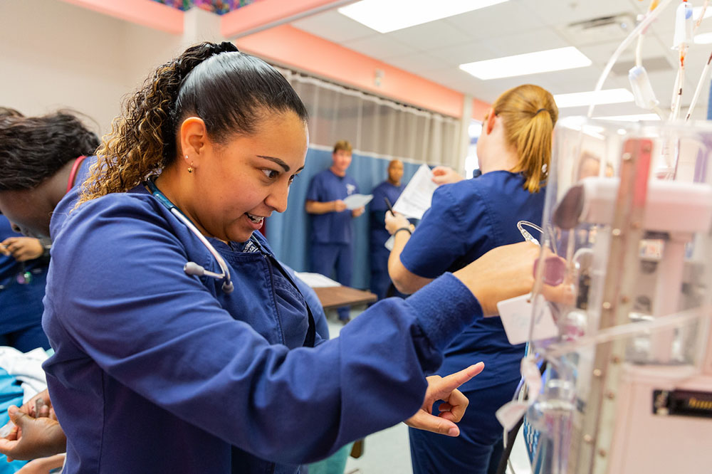 female nursing student wearing blue scrubs looking at medical equipment