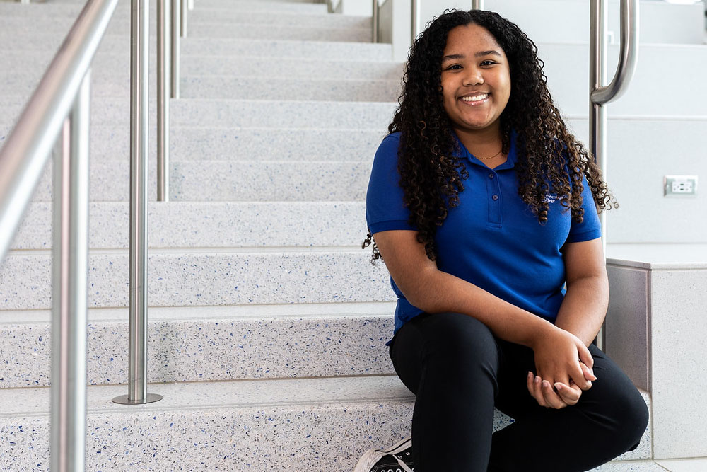 female student wearing a blue polo shirt sitting on stairs at the St Pete Gibbs Campus