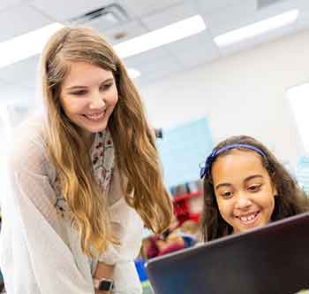 A teacher instructing a student at her laptop computer.