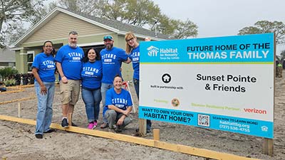group of SPC employees wearing blue Titans tshirts smiling in front of a huse they are helpung to build