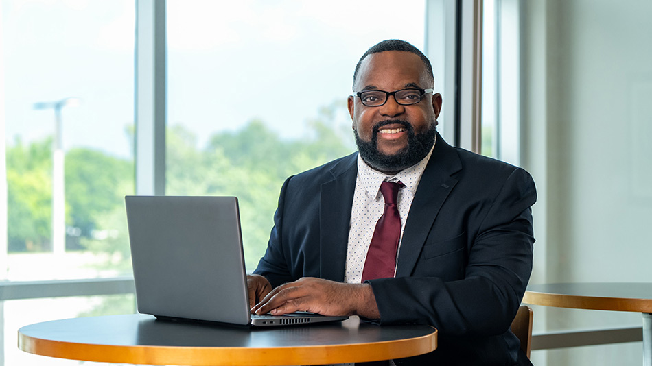 portrait of a man in a business suit sitting at a laptop in front of a window