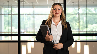 female student with long blonde hair, in a black suit jacket, holding a laptop