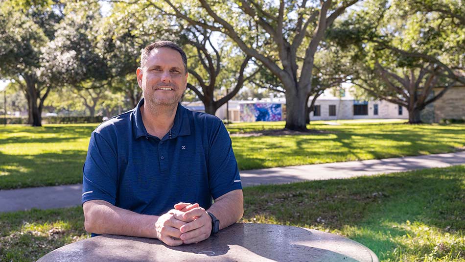 baseball player and SPC alum Jeff D’Amico sitting at a concrete table wearing a blue shirt with his hands folded