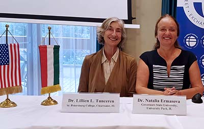 Doctors Tunceren and Ermasova seated at a table behind their nameplates and beside the USA and Hungary flags.