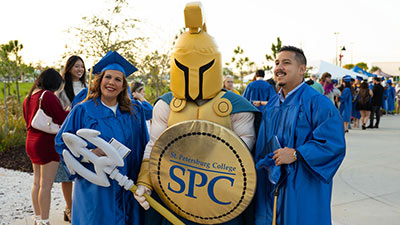 female and male graduates in cap and gown celebrating graduation at BayCare Sound with Titus the Titan mascot
