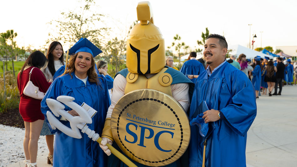 female and male graduates in cap and gown celebrating graduation at BayCare Sound with Titus the Titan mascot