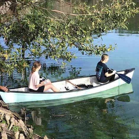 two students keeping pinellas beautiful pciking up trash from a canoe on the water