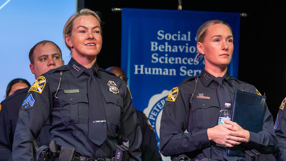 two female police officers standing on a stage in blue uniforms