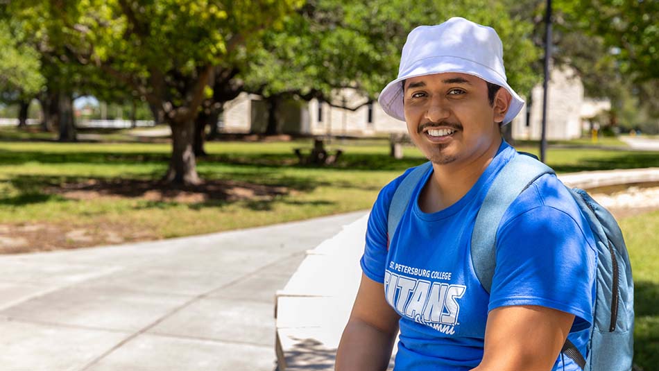 young man sitting on the Clearwater Campus wearing a blue SPC shirt and sun hat