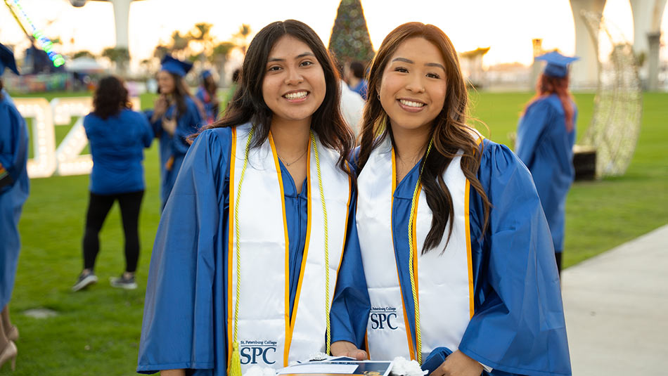 two female students with brown hair posing in their graduation gowns