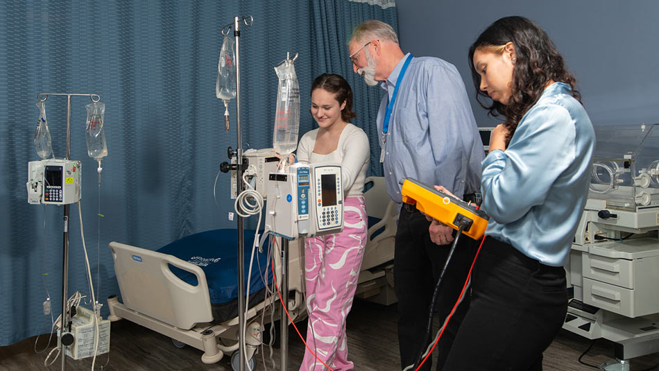 two students working on medical equipment under the direction of a professor in a tie