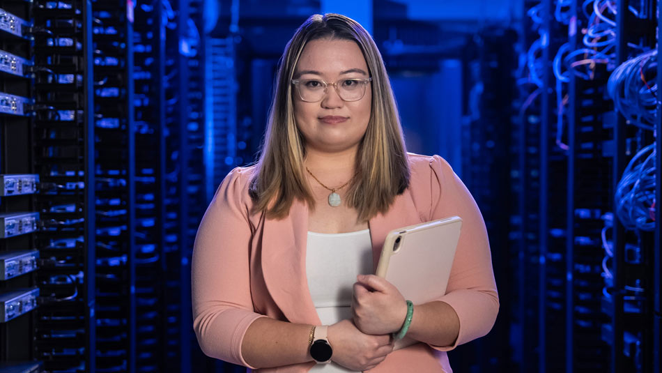 a female student holding a tablet in front of a room of servers against a blue background