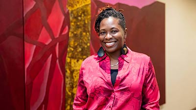 portrait of SPC alumna Dawn Grady in a pink dress shirt standing in front of a painting