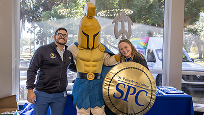 two SPC employees standing and smiling with Titus, the Titan mascot