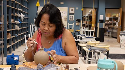 older female students holding a paintbrush while she applies color to a ceramic head