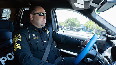 male police officer wearing a blue uniform sitting in the front seat of his patrol car