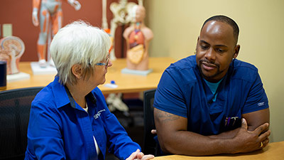 female nursing instructor working with a male nursing student in a health lab classroom
