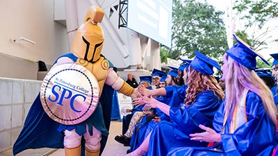 Titus the Titan mascot gives a group of graduates high fives during Spring 2025 graduation ceremony