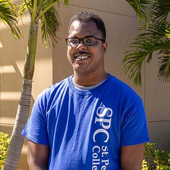 Terry Ellison, wearing a blue SPC t-shirt, posing in fornt of a campus building.