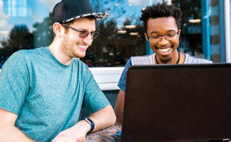 two people sitting outside, looking at a laptop