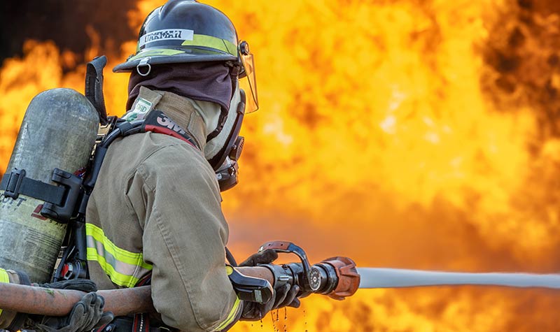 fire academy student in full gear putting out a blazing fire
