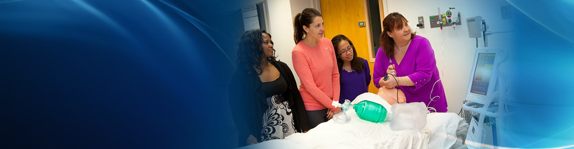 Four female students in a mock hospital room, performing respiratory care to a training manakin.