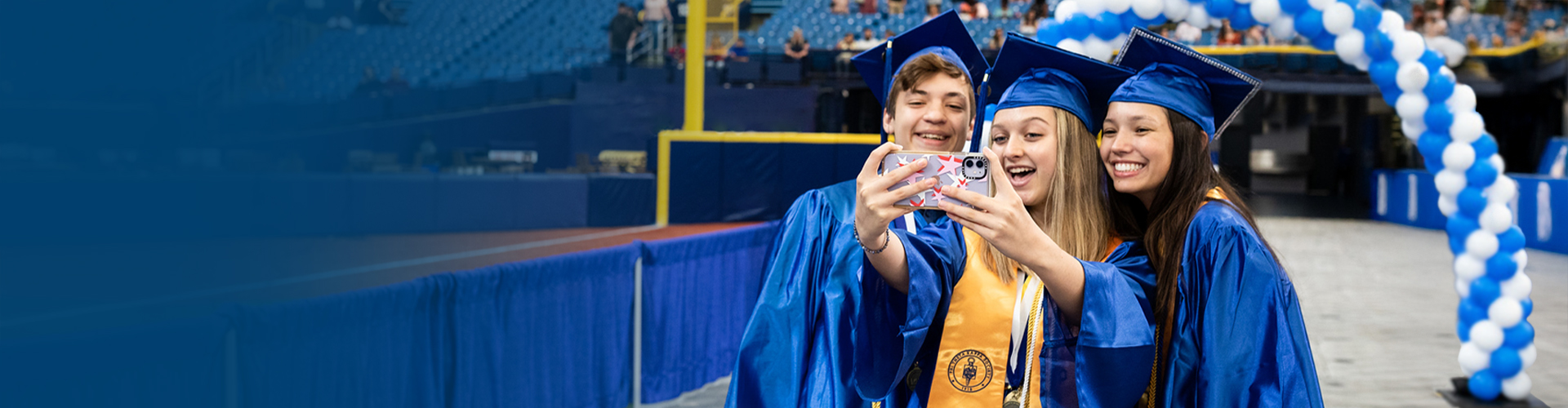 Collegiate high school students taking a selfie at graduation in their blue caps and gowns