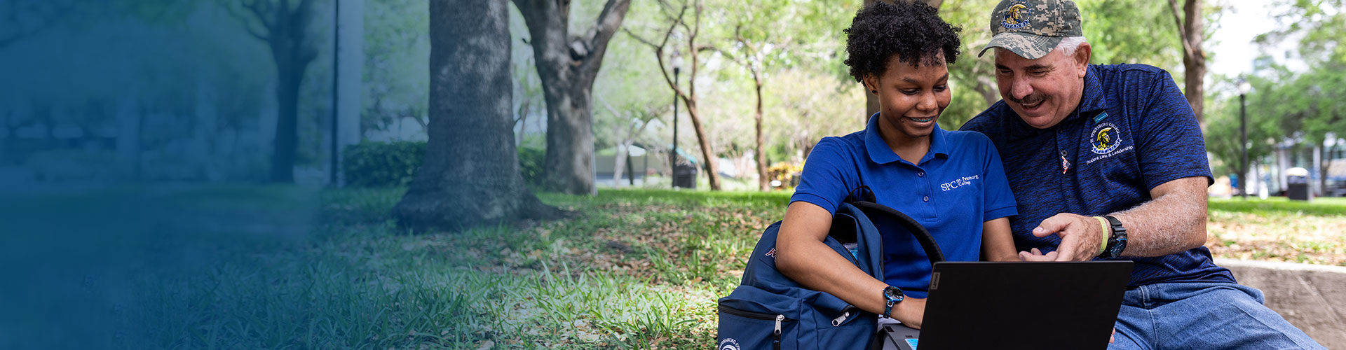 Two SPC students sitting on the campus grounds, working on a laptop