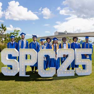 A group of new SPC graduates pose behind large letters that spell SPC 2025
