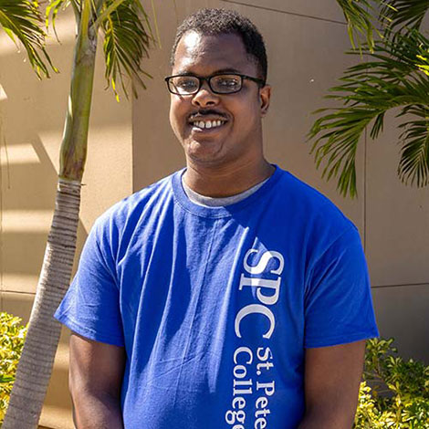 SPC alum Terry Ellison, standing in front of the palm tree landscaping of an SPC campus building, wearing a blue SPC T-shirt.
