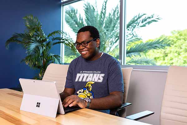 A male SPC student, wearing a Titans T shirt, sitting at a table, working on his laptop.