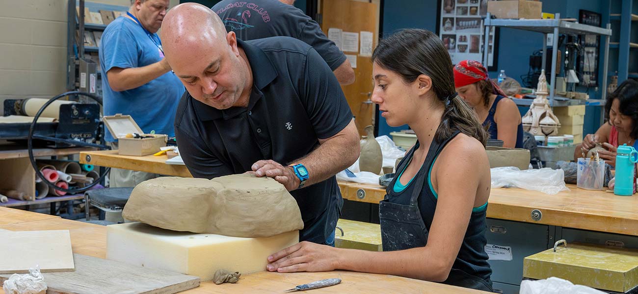 A professor and student in the ceramics lab shaping a large piece of clay.