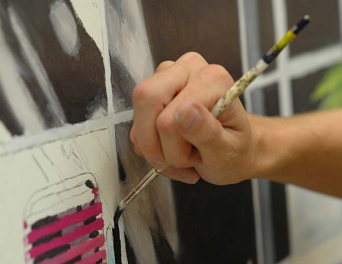 A hand, holding a paint brush, making a stroke on a canvas.