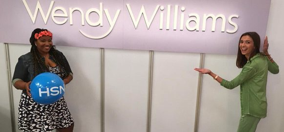 Destinee Bullard posing in front of a Wendy Williams’ fashion line sign