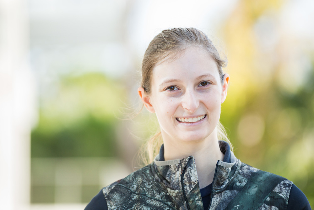 female student with blond hair in a ponytail smiling while wearing camouflage military fatigues