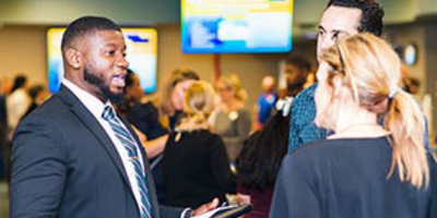 three individuals dressed in business attire speaking at a conference