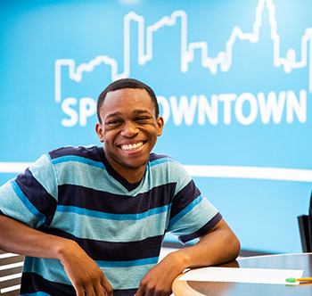 african american student in a blue striped shirt sitting in front of a blue wall with the words SPC Downtown