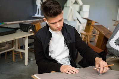 male student drawing in class while wearing ear buds