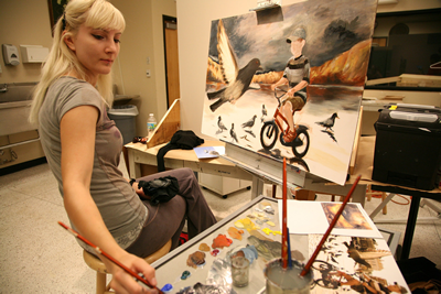 female student leaning back to grab paint brushes for her canvas