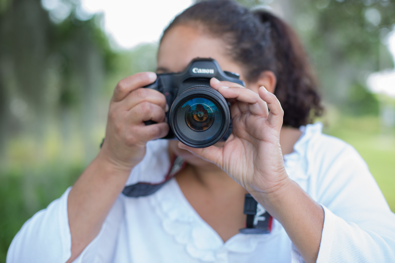 female student in a white shirt pointing a camera at the viewer